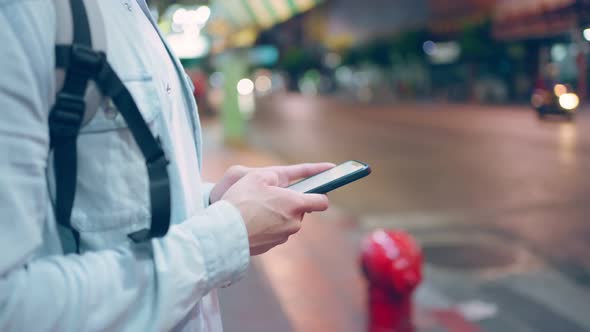 Close up of Asian man backpacker chatting on mobile phone walk in city. alt