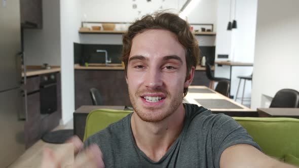 Smiling Young Man Making Selfie or Video Call While Sitting at Home on Sofa. Portrait of Male alt