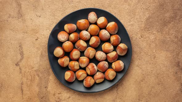 Hazelnuts in shells are falling onto a black ceramic plate - stop motion alt