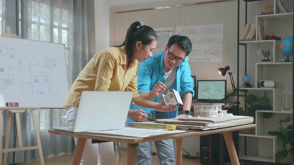 Asian Woman And Man Engineers Holding Paper Model Of House Discuss About Design At The Office alt