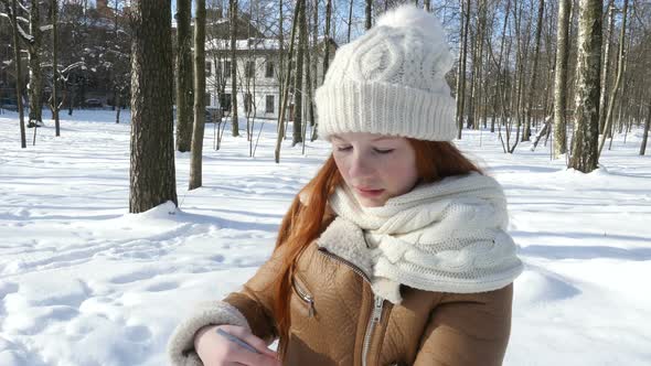 Red-Haired Teen Girl Standing At Winter Park And Draws In Sketchbook.