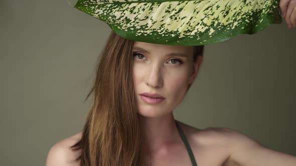 Beautiful young woman with soft and clean skin posing with tropical leaves.