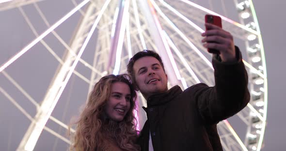 Happy couple having fun at amusement park and taking a selfie with a mobile p