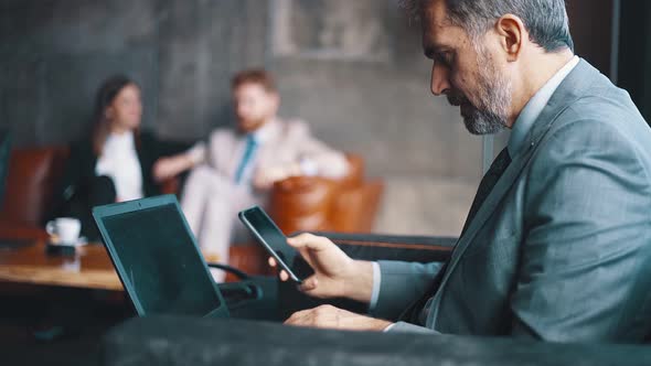 Businessman using smartphone and laptop in a lobby of a hotel