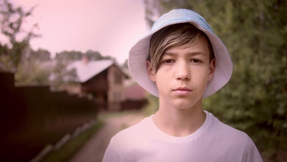 Portrait of a Serious Sad Boy in a Hat Looking at the Camera Outside in Village Cinematic Shot