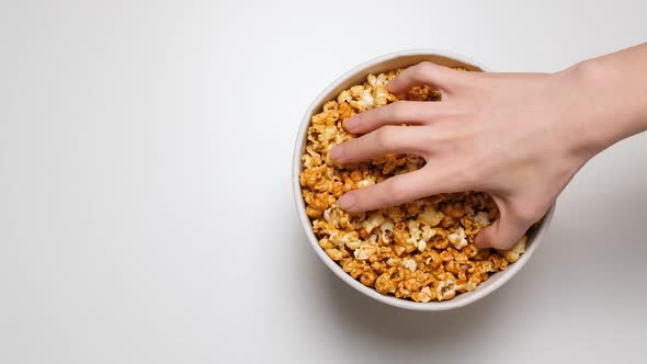 Top View on Hand Greedily Takes Popcorn From a Paper Bucket Isolated on White Background