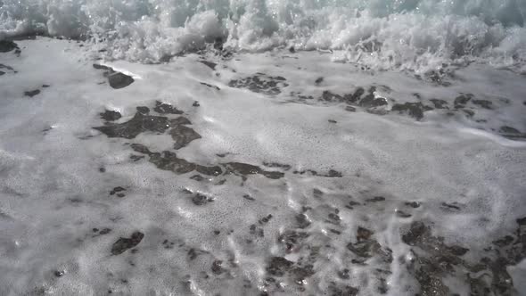 Closeup of Stormy Sea Waves with White Foam is Lapping on Pebble Beach
