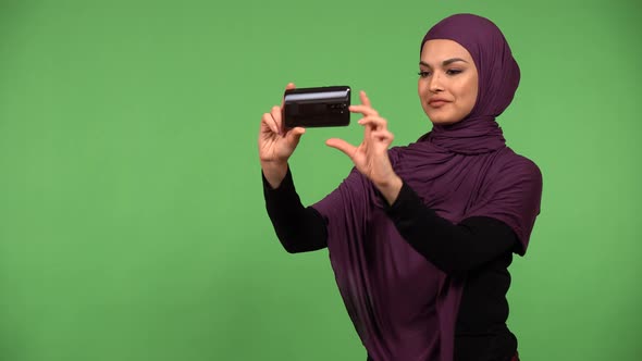 A Young Beautiful Muslim Woman Takes Pictures with a Smartphone  Green Screen Background