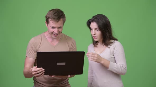 Young Man Using Laptop with Young Woman Looking Shocked alt