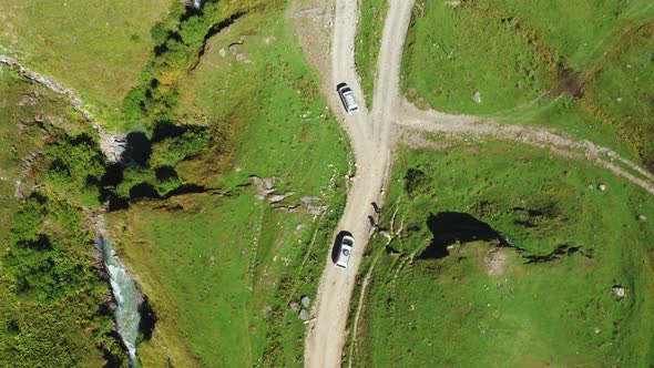 A Topdown Aerial View of of Two Cars of Travelers Driving Along a Dirt Road One After the Other alt