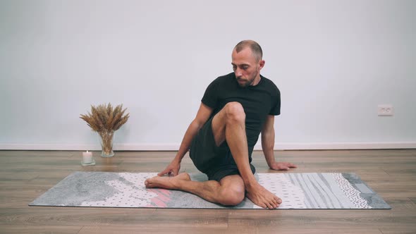 Caucasian Man Does Yoga Online A Man Sits on a Mat and Turns His Legs Half Pose of the King of