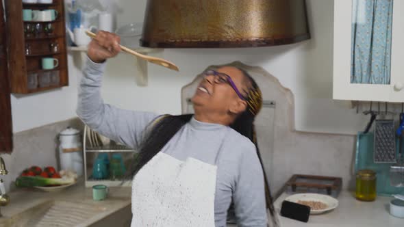 African senior woman having fun singing in the kitchen while preparing a homemade recipe alt
