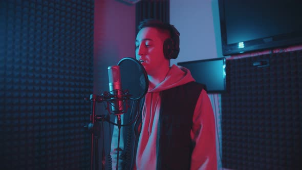 A Man in Headphones Rapping in the Studio Gesticulates While Recording His Track - Neon Lighting alt