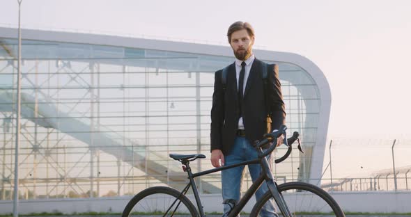 Office Worker Posing Near His Bicycle on the Big Glass Construction Background  alt