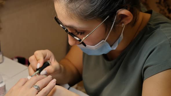 Turkish Manicurist in Big Glasses Applies Polish with a Brush to a Client alt