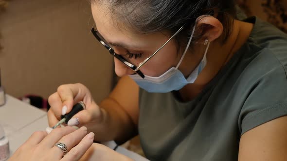 Turkish Manicurist in Big Glasses Applies Polish with a Brush to a Client