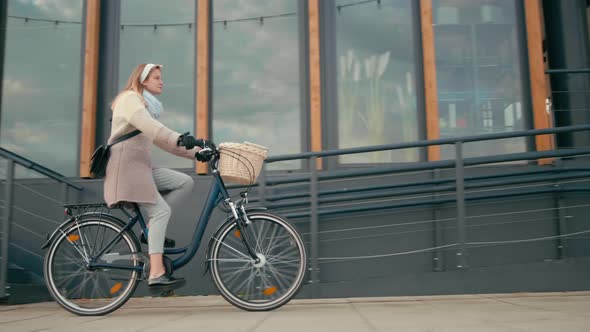 Woman Rides Bicycle in City Street with Modern Building in Cold Autumn Day