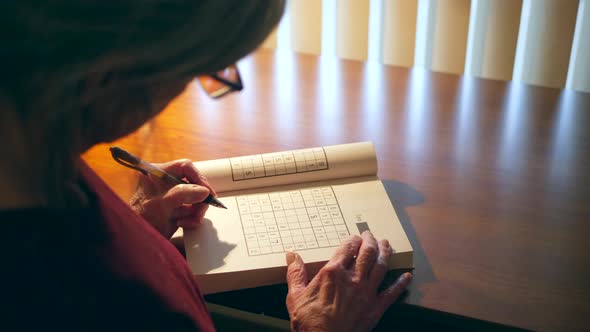 Middle aged caucasian woman with aging hands solving a number puzzle book for mind acuity to stay me alt