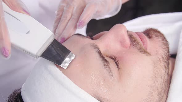 Ultrasonic Face Scrubber. Beautician Cleans the Face of a Young Man alt