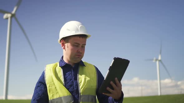 Maintenance Standing Near Wind Mill and Making Notes on Tablet alt