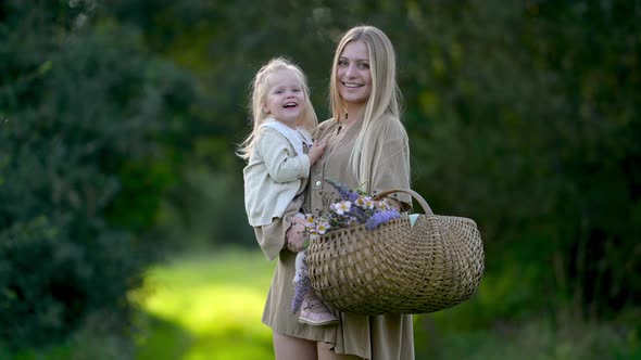 Happy young mum and daughter with wild flowers bouquet walking together outdoor