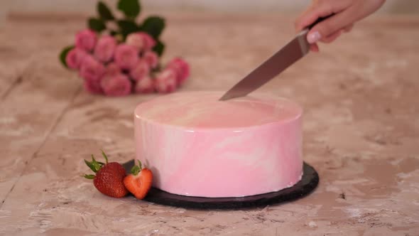 Cutting a strawberry mousse cake with pink mirror glaze.