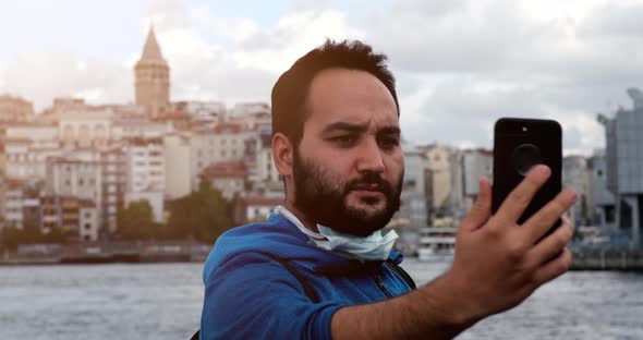 A serious man taking a selfie in front of Galata Tower in Istanbul, Turkey