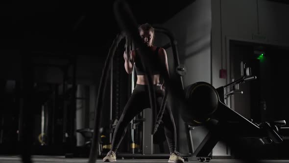 Handheld Athletic Female Performs Exercises with Battle Ropes Endurance Training in the Gym Slow alt