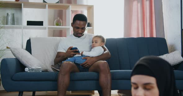 Dad Showing Cartoon on Smartphone for His Small Son while His Pretty Relaxed Active wife in hijab alt