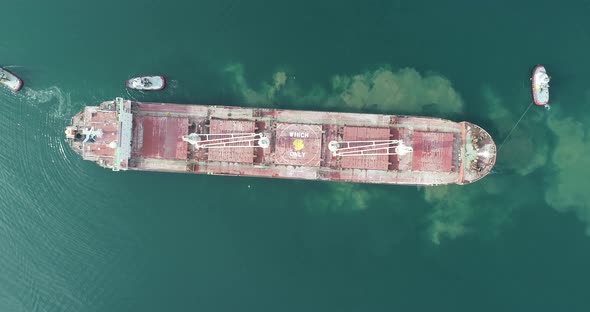 Aerial top down view of Tug boats assisting big cargo ship.  alt