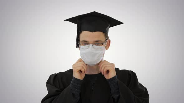 Student in Gaduation Gown and Face Mask Stumbling on Gradient Background alt