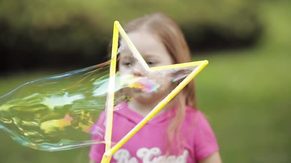 Confident Playful Little Cute Girl Blowing Huge Air Soap Bubble Blower Medium Close-up