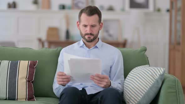 Young Man Reading Documents on Sofa  alt