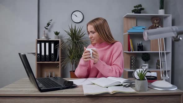 Young Girl in Knitted Sweater which Posing on Camera with Cup of Tea During Work alt