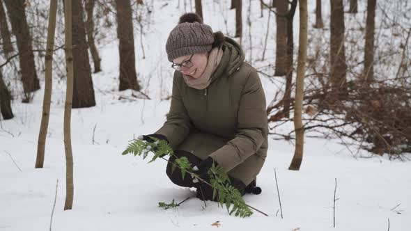 Woman in Glasses Holds in Hands with Smile Examines Green Leaves of Fern alt
