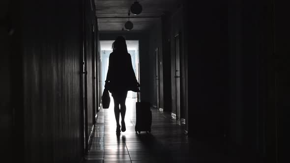 Silhouette of Businesswoman Going with Luggage along Corridor