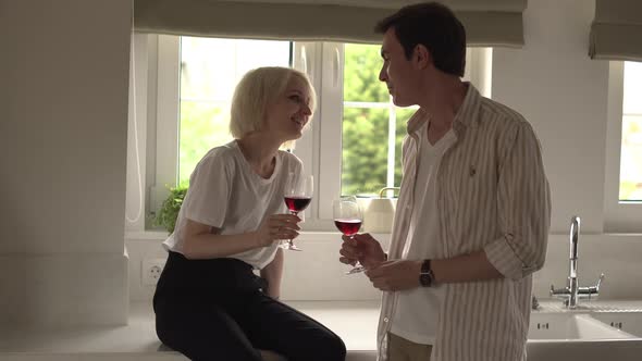 Young Couple in Love Sitting in the Kitchen Flirting and Drinking Wine alt
