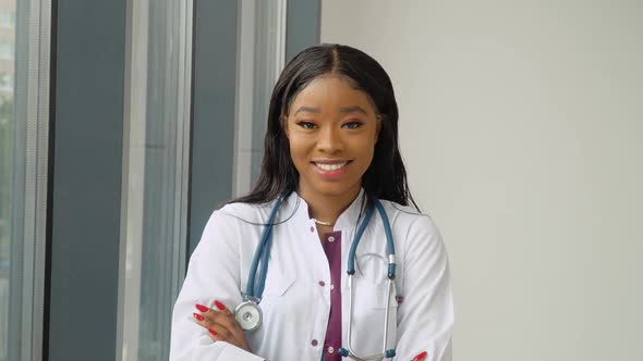 A Young African American Female Graduate in a White Medical Gown Smiles and Poses for the Camera alt