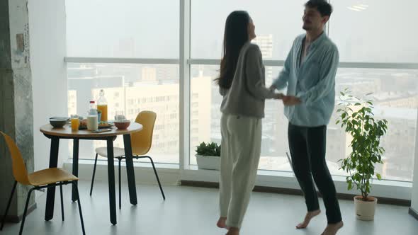 Portrait of Happy Married Couple Dancing and Hugging Indoors in Kitchen Against Panoramic Window alt