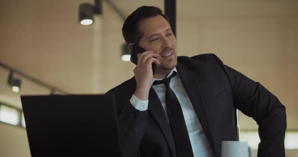 A man in a formal suit talking on the phone, while working at the office. Medium shot, slow motion. alt