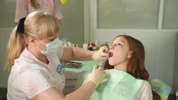 Female Dentist Doing Anesthetic Injection to Her Patient Girl in Dental Cabinet alt