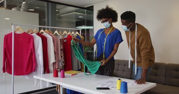 African american male and female fashion designers wearing face masks in discussion at work alt