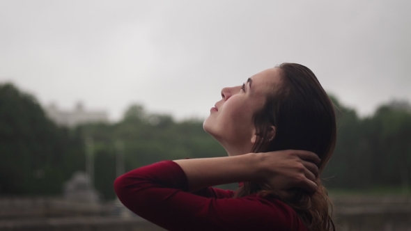 Young Woman Looking Up at Rain and Stroking Head with Wet Hair