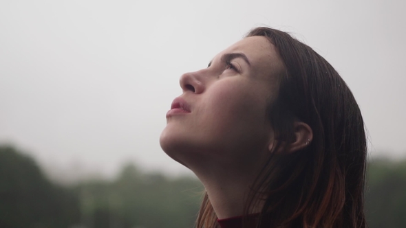 Young Sad Woman with Wet Hair Looks Up at Rain with Hope Cloudy Bad Weather