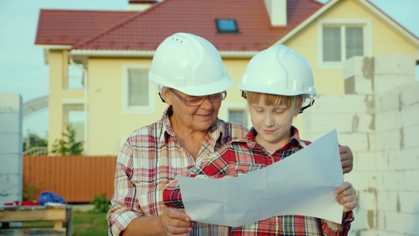 Grandmother with Her Granddaughter Is Studying the Drawing of the House Together. They Are Standing alt