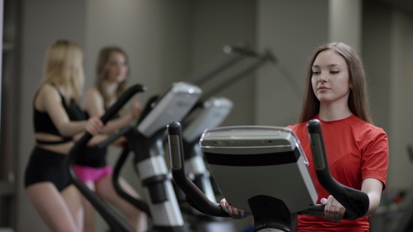 Cute Girl in Red Shirt Vigorously Work on Exercise Bike and Trainer Come Greed Her in the New Gym