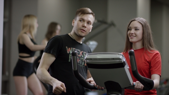 Nice Girl in Red Shirt Vigorously Work on Exercise Bike and Trainer Come Help with Motivation Her in
