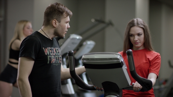 Beautiful Girl in Red Shirt Vigorously Work on Exercise Bike and Trainer Come Help with Motivation