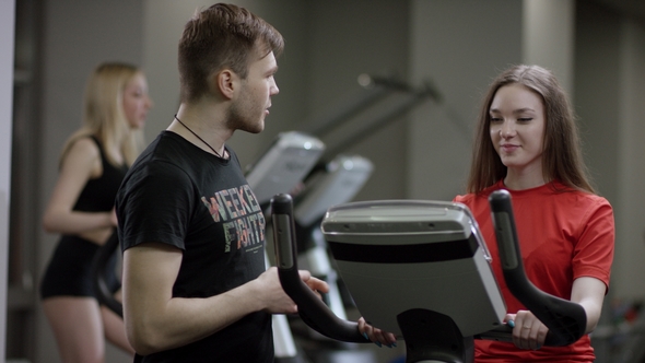 Awesome Girl in Red Shirt Vigorously Work on Exercise Bike and Trainer Come Help with Motivation Her