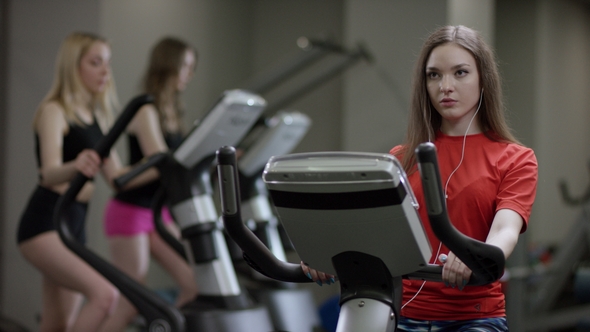 Nice Girl in Red Shirt Vigorously Works on Exercise Bike alt